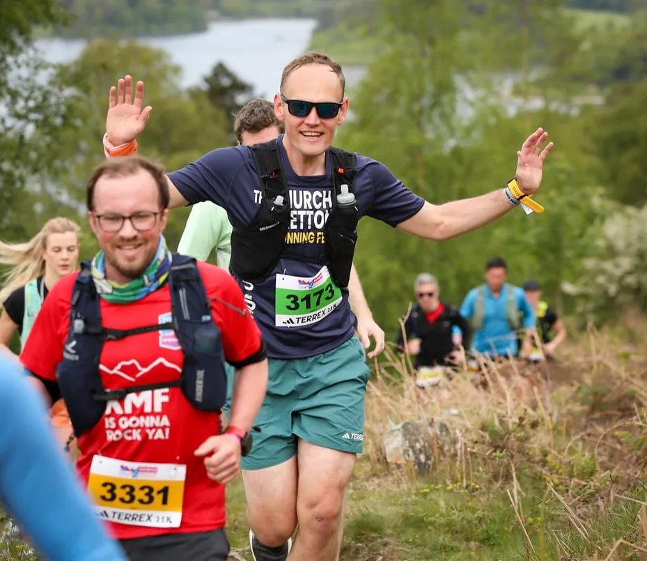 Andy running a trail race, arms out and grinning