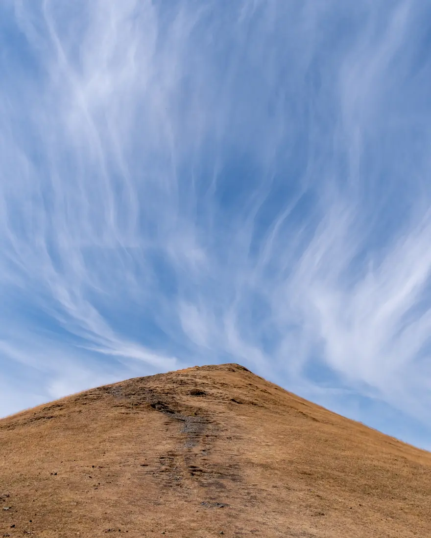 A grassy hill summit beneath streaks of cirrus cloud